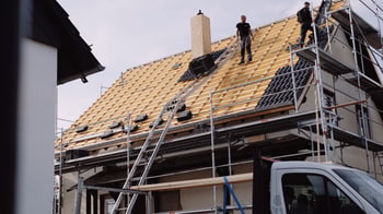 Zwei Dachdecker auf einem Gerüst montieren schwarze Solarpaneele auf einem neuen Holzdach.