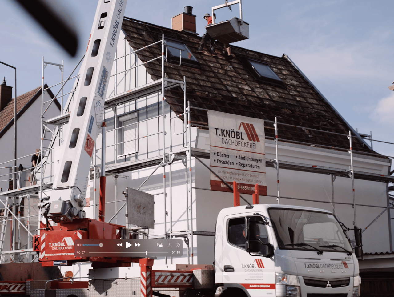Haus mit Gerüst und Firmenschild der T. Knöbl Dachdeckerei, davor ein Kranwagen