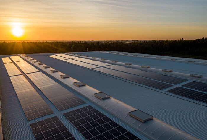 Solarpaneele auf einem großen Hallendach bei Sonnenuntergang.