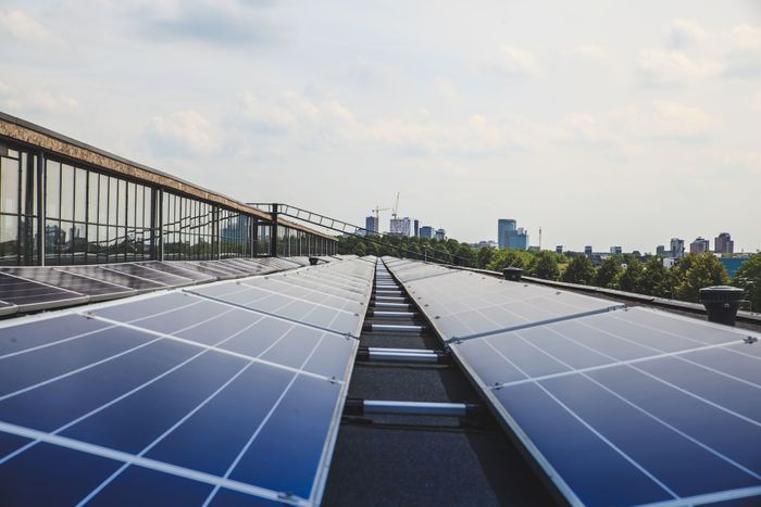 Blaue Solarmodule auf einem flachen Dach mit Stadtansicht im Hintergrund.