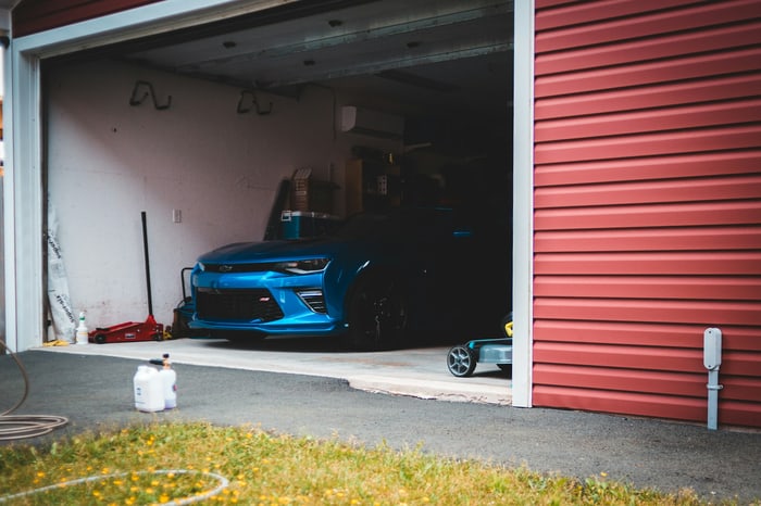 Ein blaues Chevrolet Camaro Sportauto steht in einer offenen Garage mit roter Außenwand.