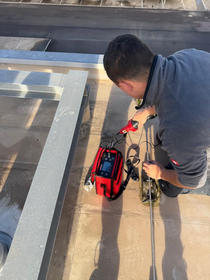 Dachdecker kniet mit einem roten Messgerät auf einem Flachdach