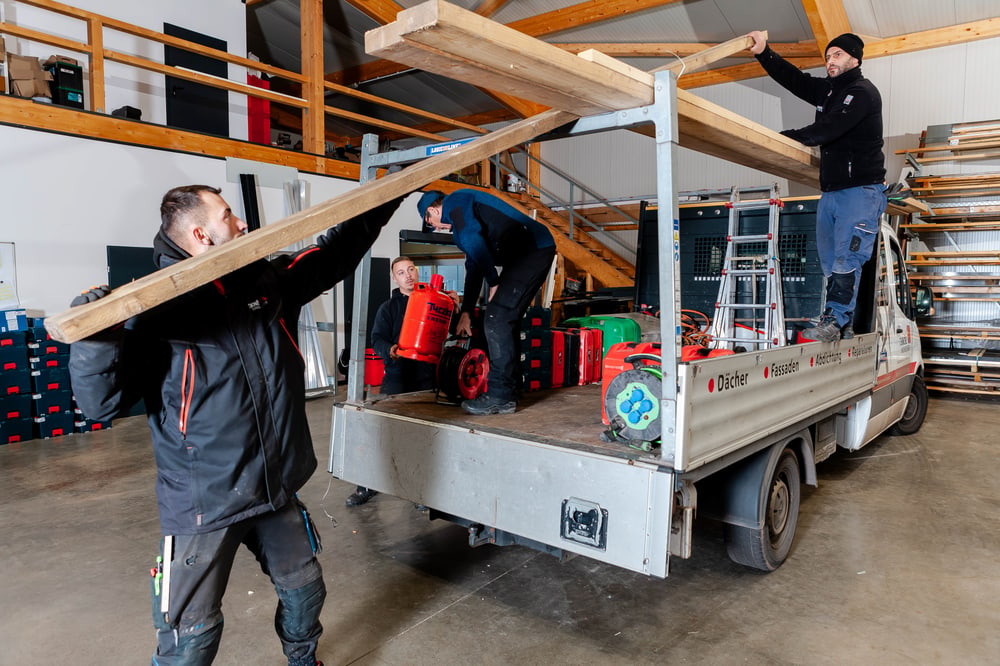 Drei Männer beladen einen Transporter mit Holzbrettern und Werkzeugen.