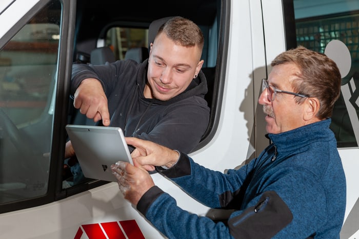 Zwei Männer schauen auf ein Tablet, einer sitzt im Transporter und zeigt auf den Bildschirm.