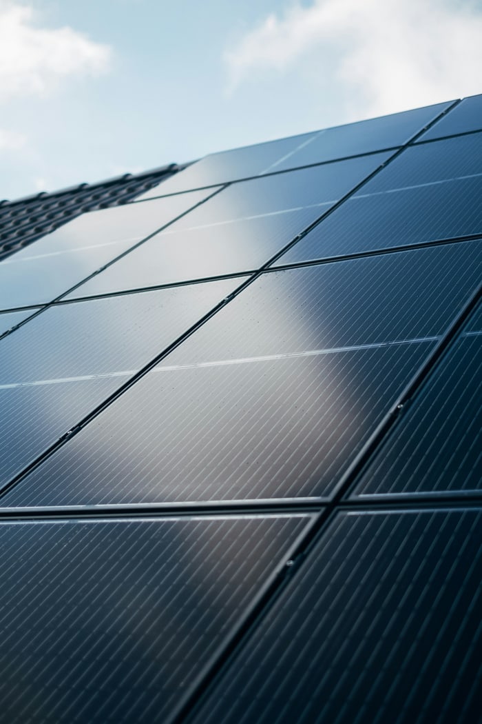 Dunkelblaue Solarmodule auf einem Hausdach unter bewölktem Himmel.