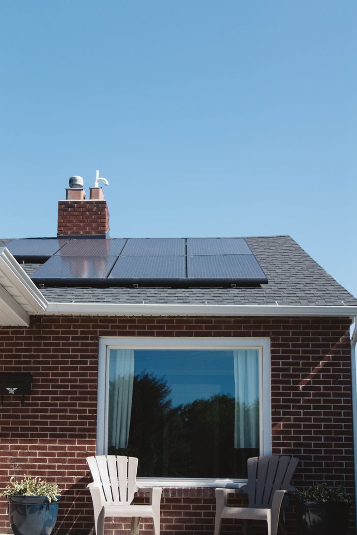 Ziegelsteinhaus mit grauen Dachschindeln, Solarpaneelen und einem Schornstein unter blauem Himmel.