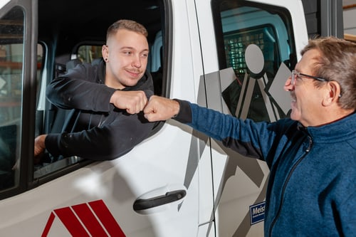 Zwei Männer machen einen Faustgruß am Fenster eines weißen Lieferwagens.