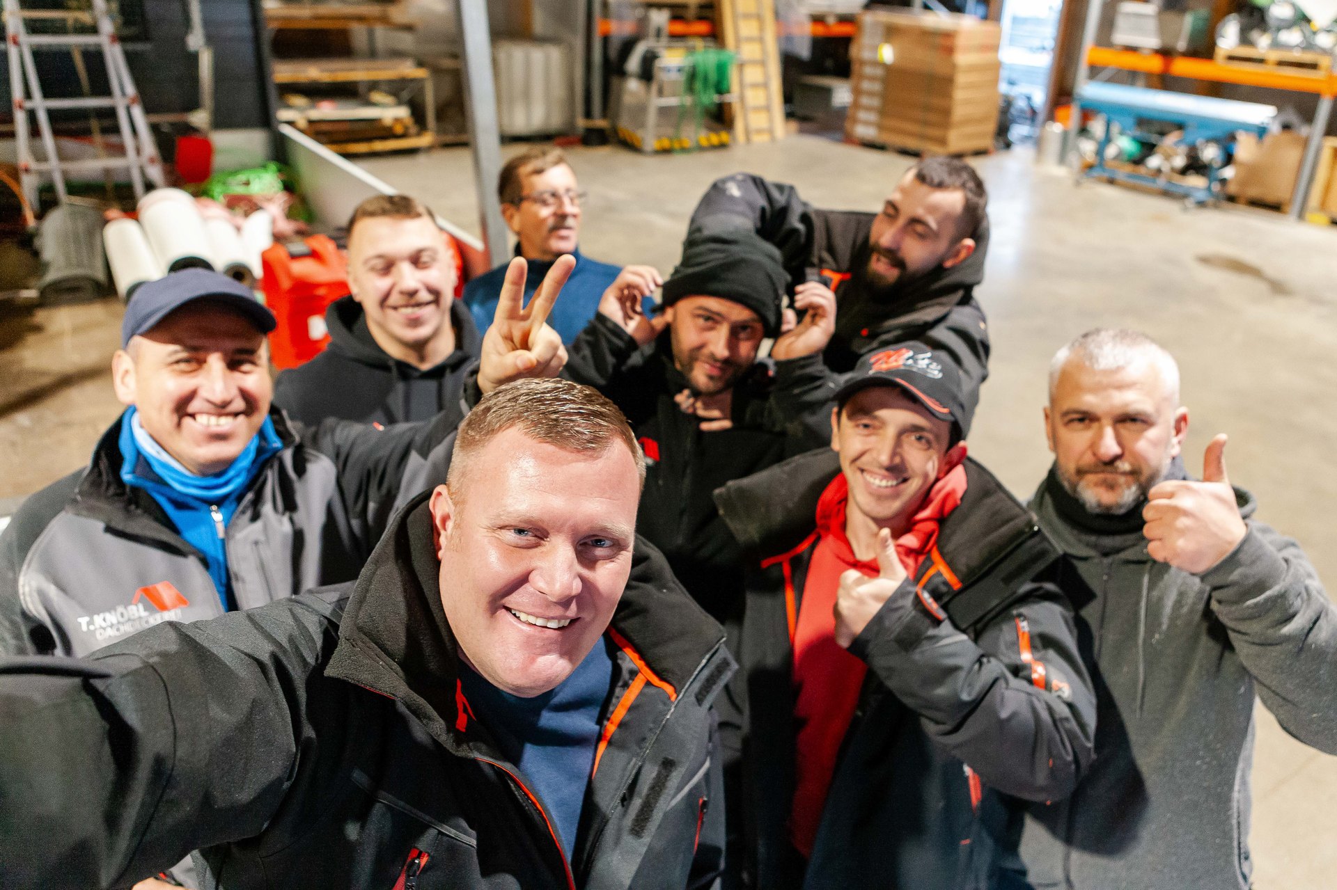 Sieben Bauarbeiter machen ein Selfie in einer Lagerhalle.