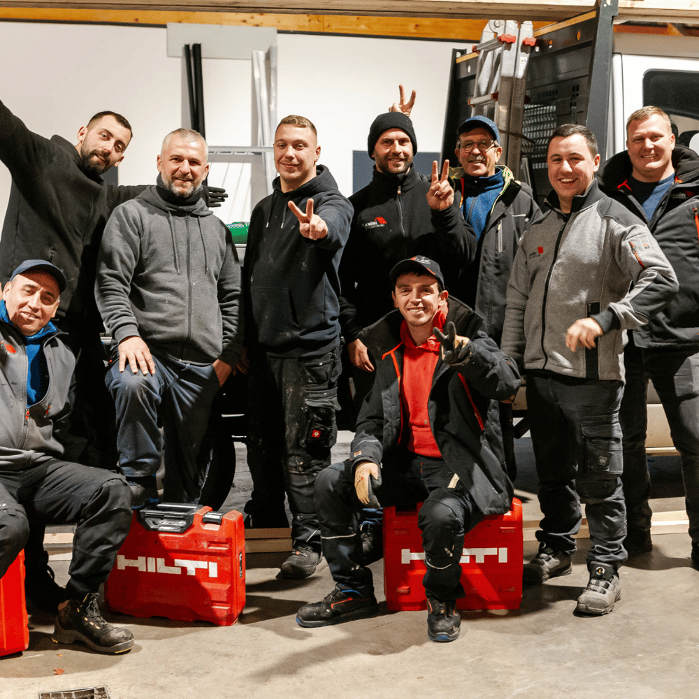Eine Gruppe von zehn Bauarbeitern posiert lächelnd, einige zeigen ein Friedenszeichen, mit roten Hilti-Werkzeugkoffern.