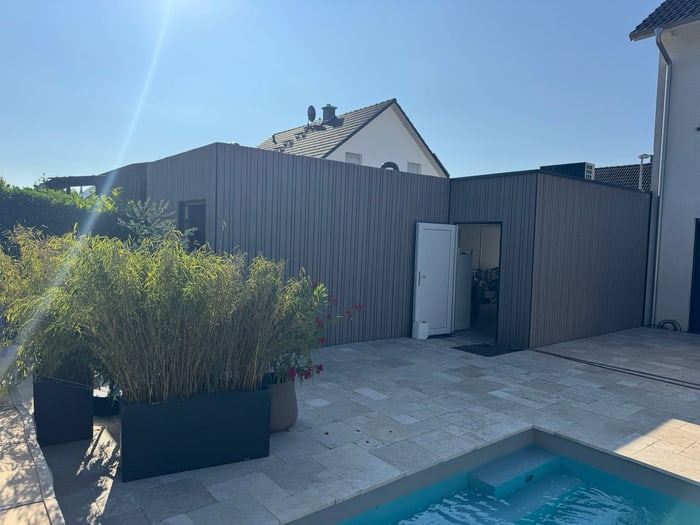 Braune Holzverkleidung auf der Rückseite eines Hauses mit offener Tür, einem Pool und Pflanzen.