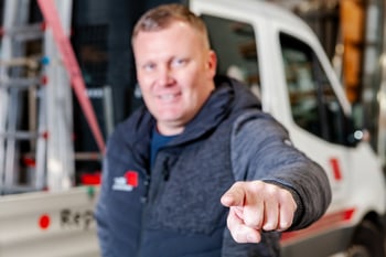 Mann vor einem Transporter zeigt mit dem Finger in die Kamera